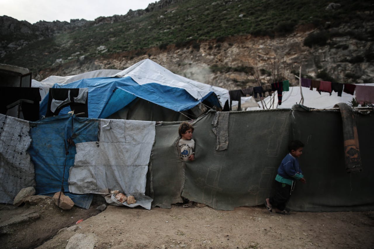 Two children outside tents in a refugee camp in Idlib, Syria, showing the harsh living conditions.