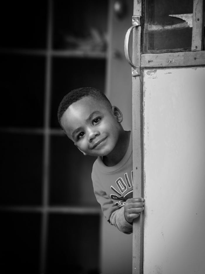 Black and white photo of a young child peeking around a door, captured in Jos, Nigeria.